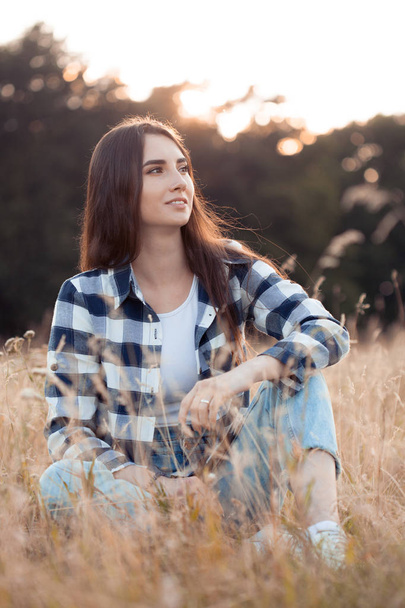 Young beautiful woman in plaid shirt sitting in grass outdoors - Foto, Imagem