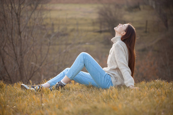 Beautiful young woman sitting on the grass in autumn - 写真・画像