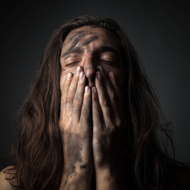 Портрет нещасного молодого чоловіка в сажі. Руки на обличчі
 - Фото, зображення