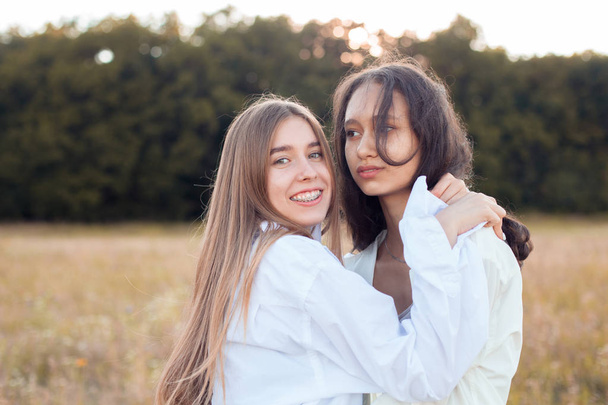 Two young women in white shirts hugging outdoors - Fotoğraf, Görsel