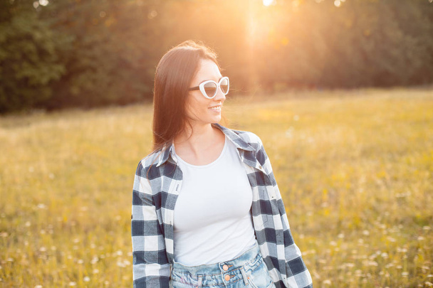 Young woman with sunglasses walking on the field under sunlight - Foto, Bild
