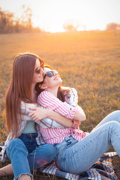 Two young women sitting on the grass and laughing at sunset. Best friends - Foto, Imagem