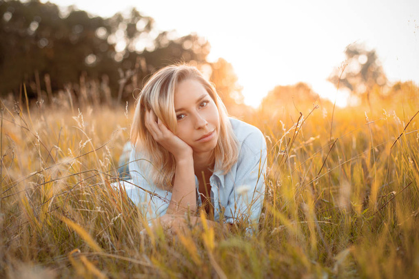 Adorable young woman lies in the dry grass at sunset. - Foto, afbeelding