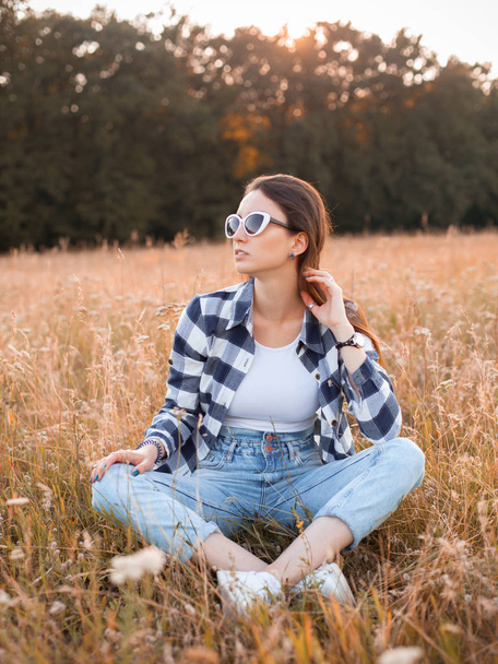 Young woman in plaid shirt is sitting on the dry grass - Φωτογραφία, εικόνα