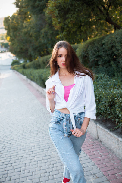 Attractive young woman in white shirt walking in the city under sunlight - Fotografie, Obrázek