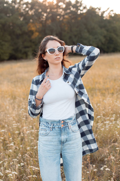 Beautiful young woman in plaid shirt and sunglasses walking outdoors. - Foto, Imagem