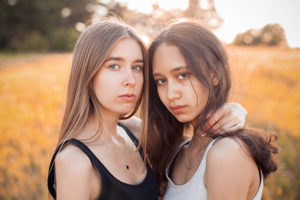 kaksi nuorta tyttöä poseeraa pellolla auringonlaskun aikana
 - Valokuva, kuva