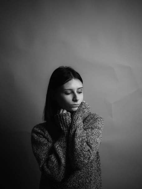 Smutná mladá žena ve svetru na šedém pozadí. Černá a bílá - Fotografie, Obrázek