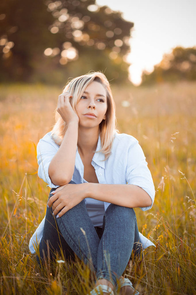 Young woman sitting on dry grass under sunlight - Fotoğraf, Görsel
