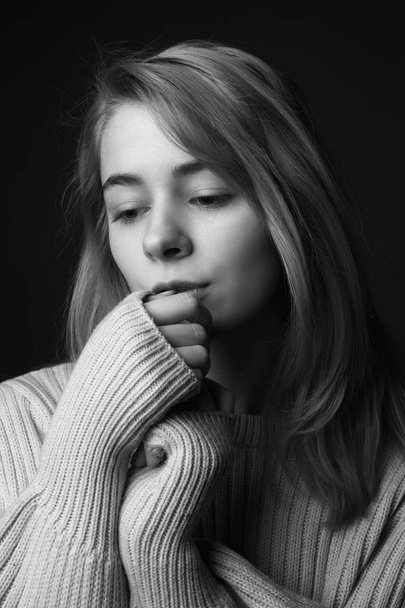 Thoughtful young woman on black background. Black and white - 写真・画像