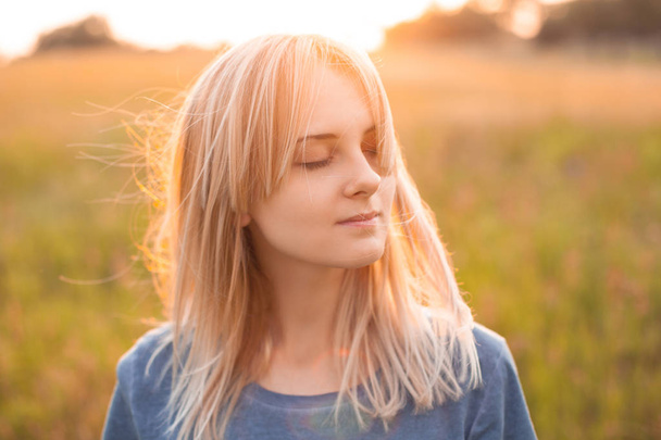 Jonge vrouw met gestreken blond haar buiten bij zonsondergang. Sluiten.. - Foto, afbeelding