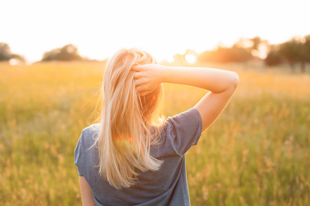Nuori nainen vaaleat hiukset seisoo kentällä ja katselee auringonlaskua
 - Valokuva, kuva