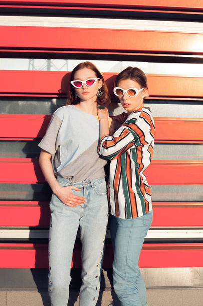 Two fashionable young women posing in the ciry on the orange background - Photo, Image