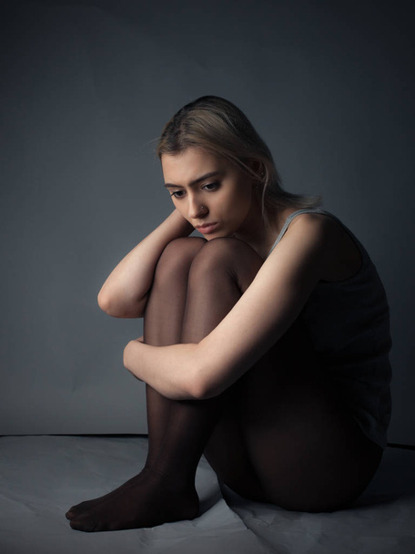 Sad girl in tights and shirt sitting on the floor - Foto, Imagen