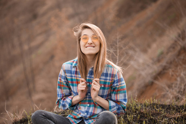 glückliche junge Frau, die im Herbst auf der Klippe sitzt und lächelt - Foto, Bild