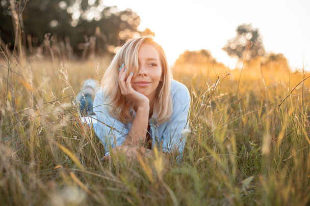 Beautiful young woman lying on the grass under light of sunset - Foto, afbeelding