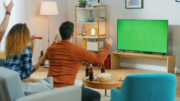 Three Sports Fans Sitting on a Couch in the Living Room Watch Green Chroma Key Screen TV Important Match, Using Horns, Cheering For their Team and Celebrates Win Doing YES Gesture. - Foto, imagen