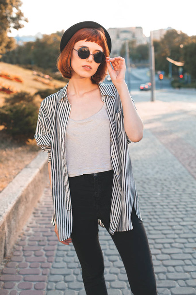 Young fashionable woman in sunglasses walking down the street at evening - Foto, Bild