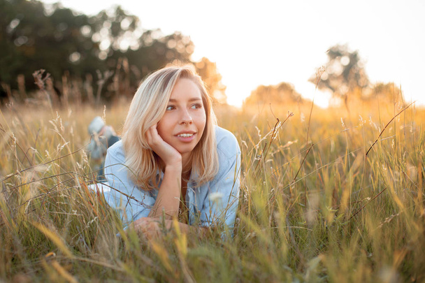 Beautiful young woman lying on the grass at sunset - Foto, Bild