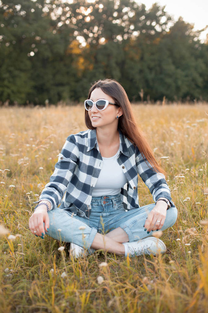 Young woman in sunglasses sitting on the grass. - Φωτογραφία, εικόνα