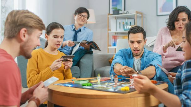Diverse Group of Guys and Girls Playing in a Strategic Board Game with Cards and Dice. Cozy Living Room in a Daytime - Foto, imagen
