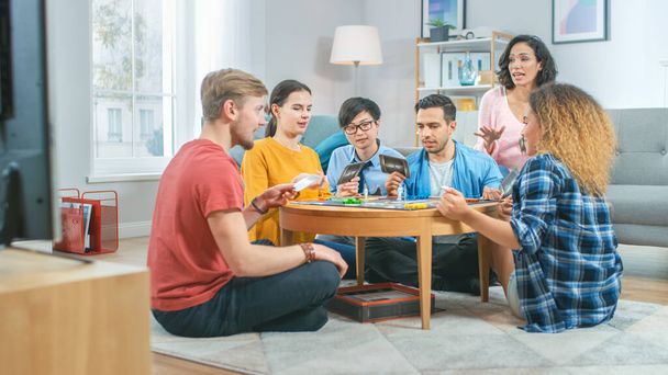 Diverse Group of Guys and Girls Playing in a Strategic Board Game with Cards and Dice. Reading Cards and Laughing. Friends Having Fun. Cozy Living Room in a Daytime - Φωτογραφία, εικόνα