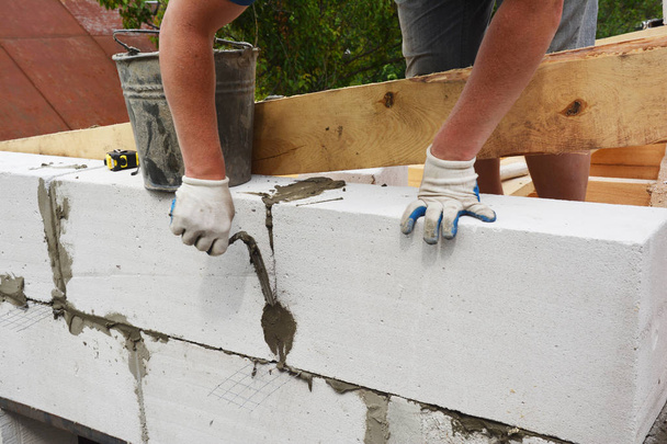 Bricklayer builder laying autoclaved aerated concrete blocks for house wall near unfinished roof wooden beams. - Photo, Image
