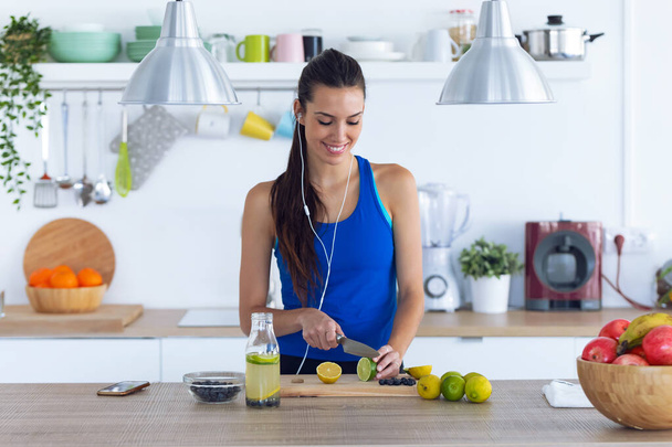 Sportos fiatal nő vágás lime miközben zenét hallgat a konyhában otthon - Fotó, kép