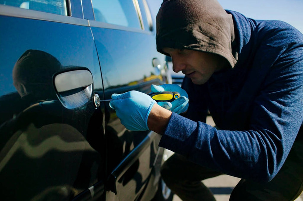 A robbery is breaking the law, hacks the lock on the car to get inside. - Photo, Image