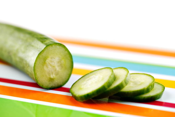 Partly sliced organic cucumber on a stripy colorful ceramic plate - Φωτογραφία, εικόνα