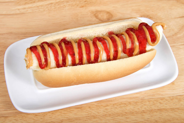 Banana with peanut butter and jelly in a hot dog bun served on a white rectangular plate served on a wood table. Top view from an angle - Photo, Image