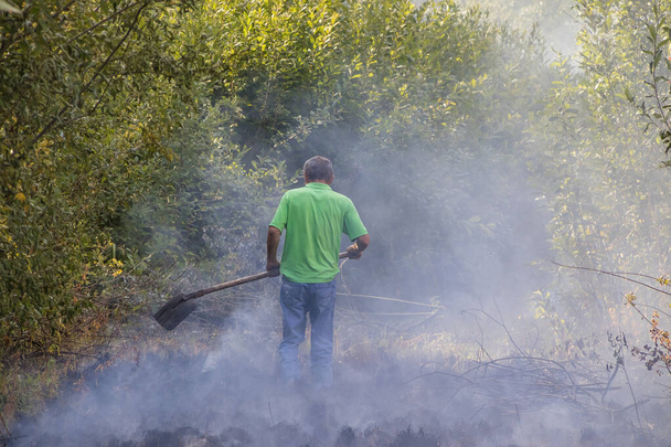 Ο άνθρωπος ρίχνει μια φωτιά με ένα γεωργικό εφαρμογή - Φωτογραφία, εικόνα