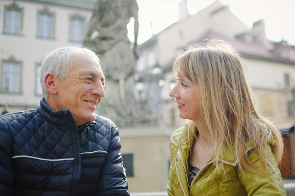 Knappe oudere man omarmt zijn jonge blonde vrouw brengt tijd samen door in de buitenlucht in de oude stad in het vroege voorjaar of de herfst. - Foto, afbeelding