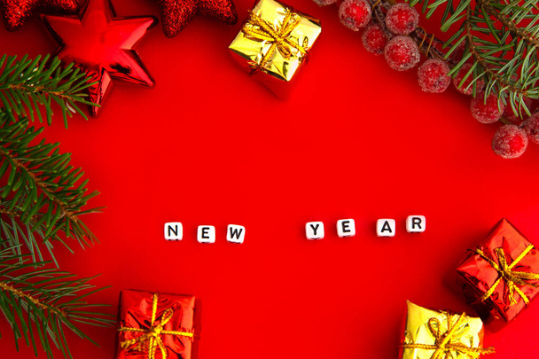 grüne Kiefernzweige mit rotem Weihnachtsspielzeug, Geschenkschachteln, roten Eisbeeren und der Aufschrift Neujahr auf Würfeln auf rotem Hintergrund. Neujahrskonzept. Platz für Text - Foto, Bild