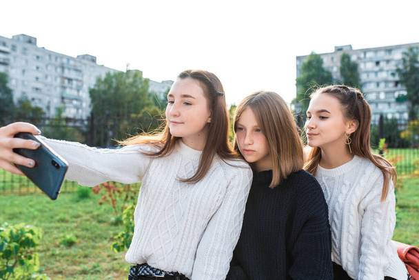 Teenage girls in summer autumn spring in city, take pictures on smartphone, on-line application on Internet video call, girlfriends relax on break at weekend after school. - Фото, изображение