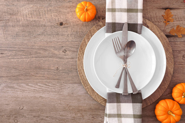 Thanksgiving or fall harvest table setting with plate, silverware, check print napkin, pumpkins and leaves. Top view, side border against a wood background with copy space. - Foto, imagen