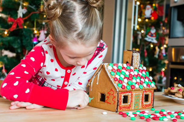Dívky dělat vánoční perník dům u krbu ve zdobeném obývacím pokoji. - Fotografie, Obrázek
