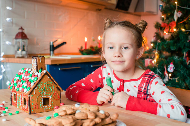 Kleine Mädchen basteln Weihnachts-Lebkuchenhaus am Kamin im geschmückten Wohnzimmer. - Foto, Bild