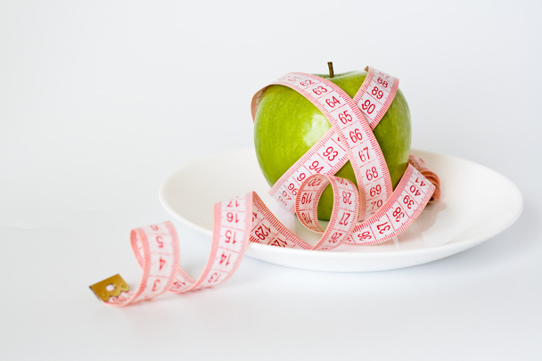 Green apple and measuring tape on a white plate - Fotoğraf, Görsel