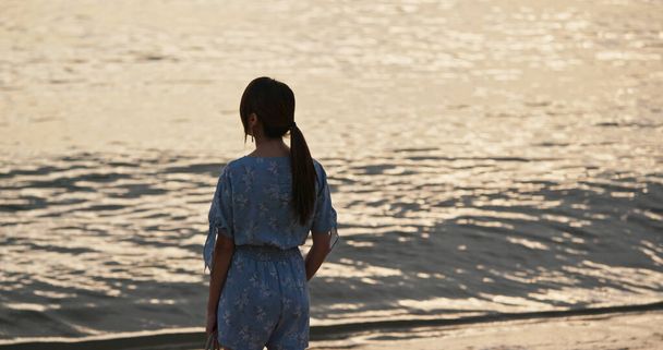 Žena stojí na pláži a vychutnat si výhled na moře při západu slunce - Fotografie, Obrázek