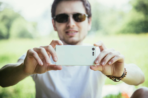 Man in sunglasses with phone on green grass outdoors - Fotografie, Obrázek