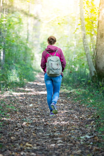 Mujer con mochila caminando en bosque otoñal. Las hojas se caen.
.   - Foto, Imagen