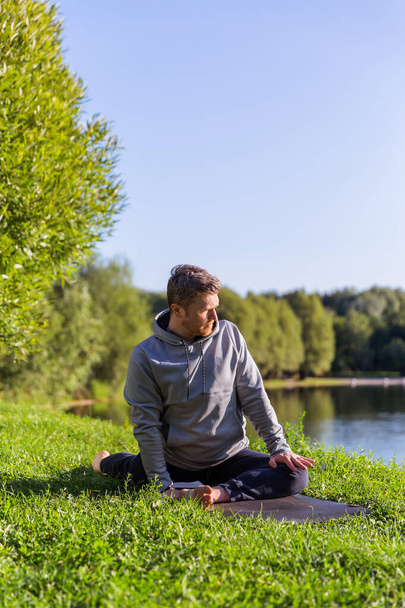 Inspired man doing yoga asanas in city park. Fitness outdoors and life balance concept. - 写真・画像