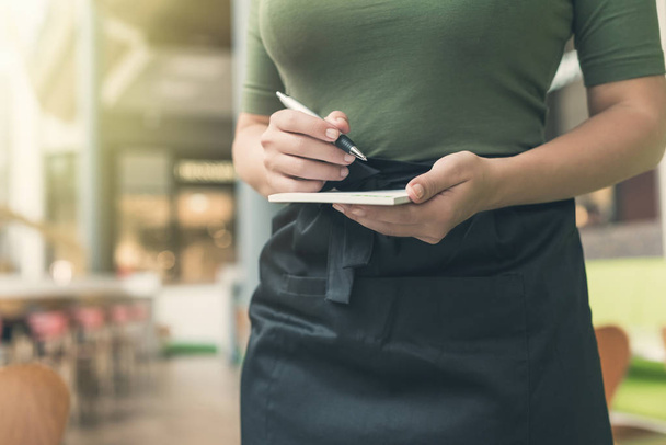 Cropped image of woman waitress in apron ready to take order using notepad and pen in cafe or restaurant.  - Foto, afbeelding