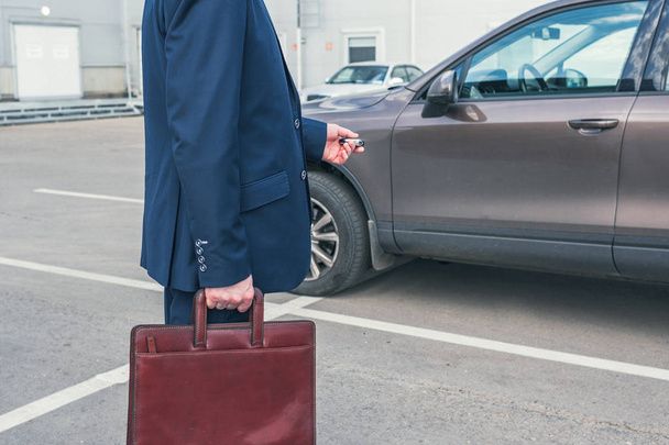 Hombre de negocios de mediana edad de pelo gris con un traje azul y un maletín pulsando el botón en la llave del coche de control remoto
 - Foto, imagen