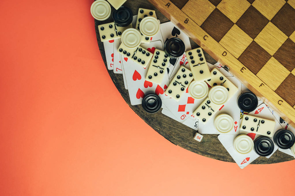 Various board games chess board, playing cards, dominoes on a old wooden table peach background. - Photo, Image