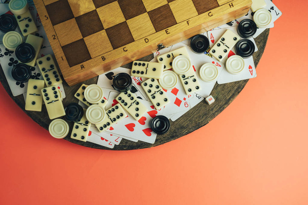 verschiedene Brettspiele Schachbrett, Spielkarten, Dominosteine auf einem alten Holztisch Pfirsichhintergrund. - Foto, Bild