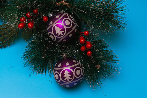 Two purple festive balloons with the image of a Christmas tree and snowflakes lie on artificial branches of a spruce, blue background, flatlay - Zdjęcie, obraz