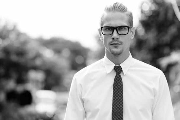 Fiatal, jóképű üzletember szemüveget visel a szabadban, fekete-fehér ruhában. - Fotó, kép