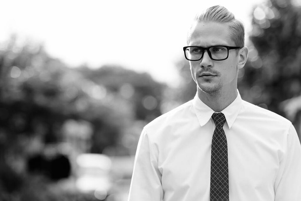 Fiatal jóképű üzletember gondolkodik, miközben szemüveget visel a szabadban - Fotó, kép